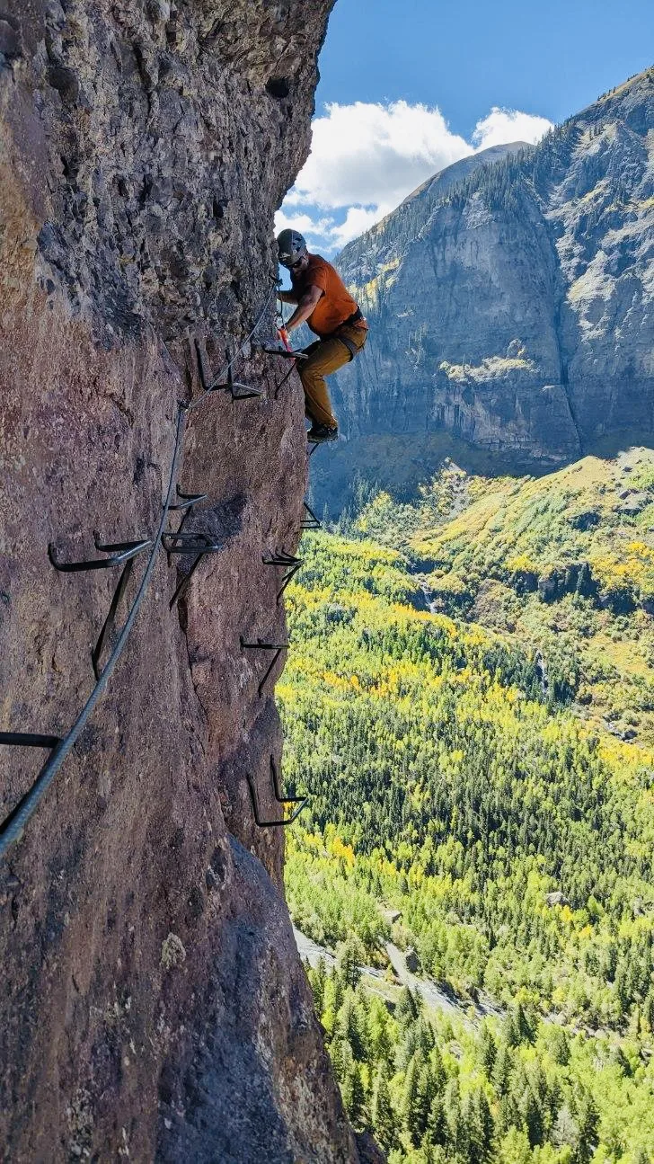 Jason climbing a via ferrata route above an aspen valley